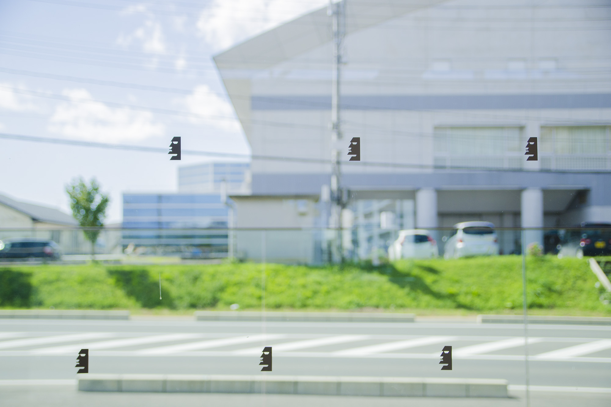 透明なガラスに黒いモアイの形のステッカーが規則的に貼られている写真