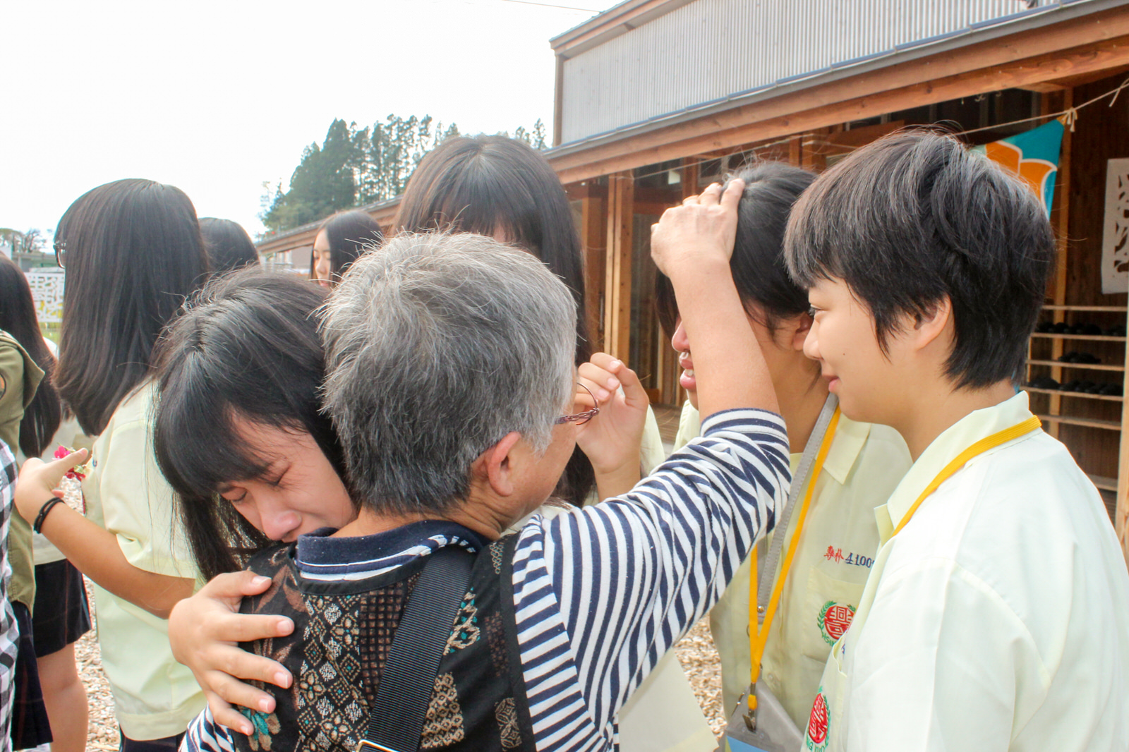 お別れの場面で年配の女性が泣いている女子学生を抱きしめて慰めている感動的な別れのシーンの写真