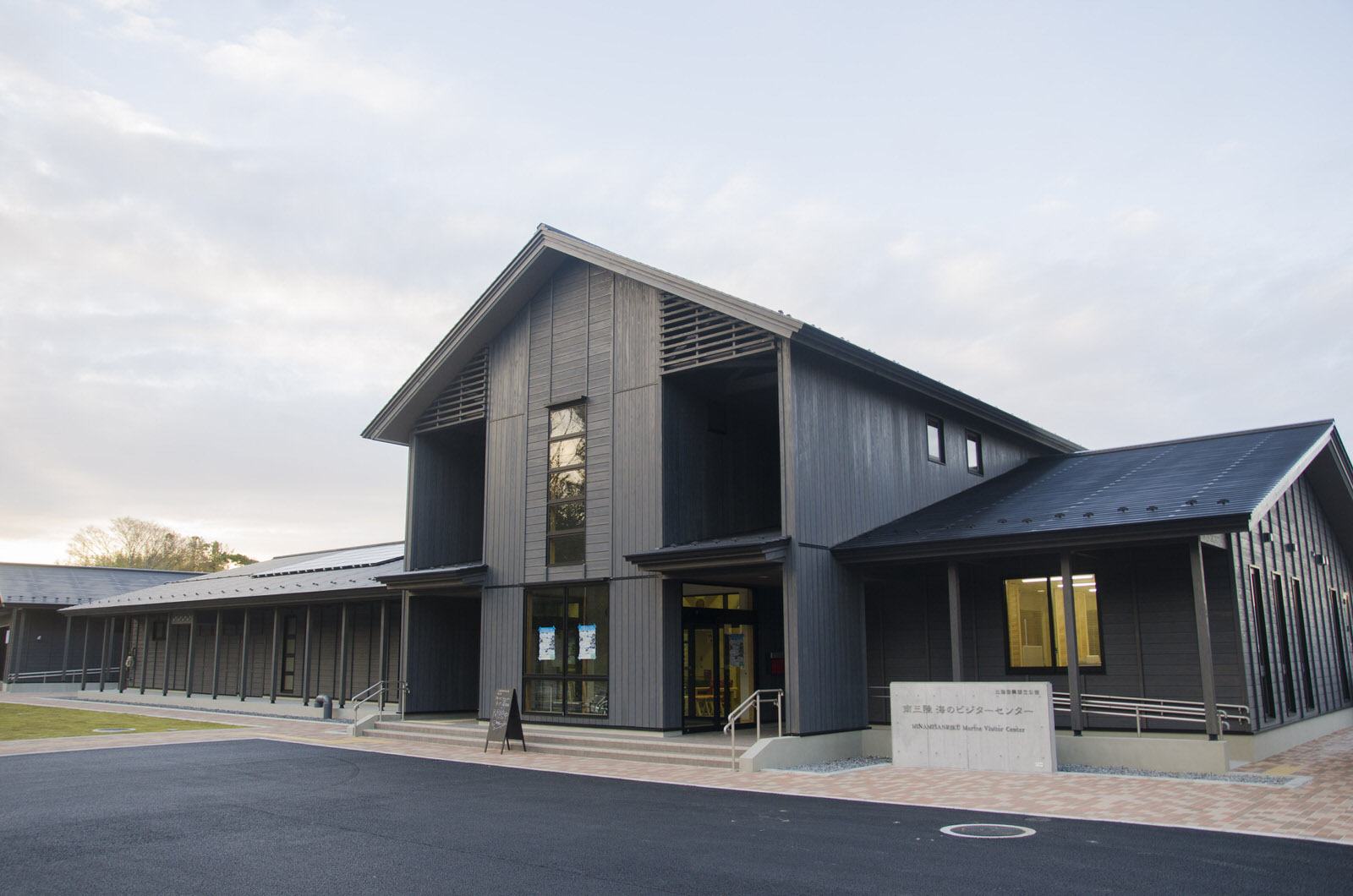 建物の右側にスロープと「南三陸・海のビジターセンター」と書かれた看板が設置され、中央に入口がある黒い外壁の木造の建物を右斜めから撮影した写真