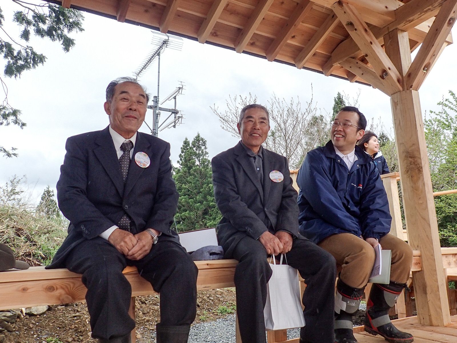木でできた東屋のベンチに3人の男性が笑顔で座っている写真