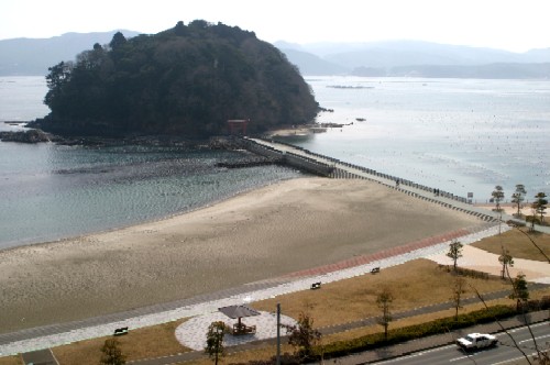 穏やかな湾内に浮かぶ緑の小島と、手前の砂浜と芝生の公園、そして島と陸地を直線で結ぶ長い橋が写し出された、広々としたサンオーレそではまの写真