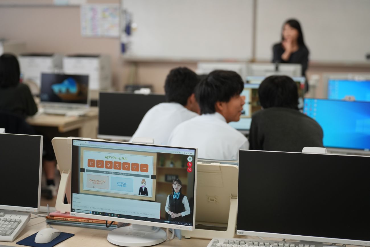 複数の学生がパソコンでAIアバターによるビジネスマナー講義をグループで受講している教室内の様子の写真