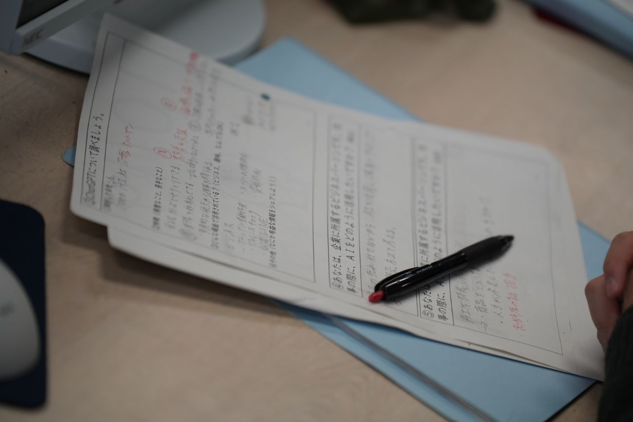 AIマナー講義のメモ用紙に赤ペンで書き込みをしながら学習している手元の写真