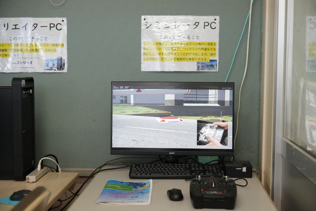 シミュレーターPCの説明書きの下にドローン操作のシミュレーション画面と送信機が置かれた机の写真