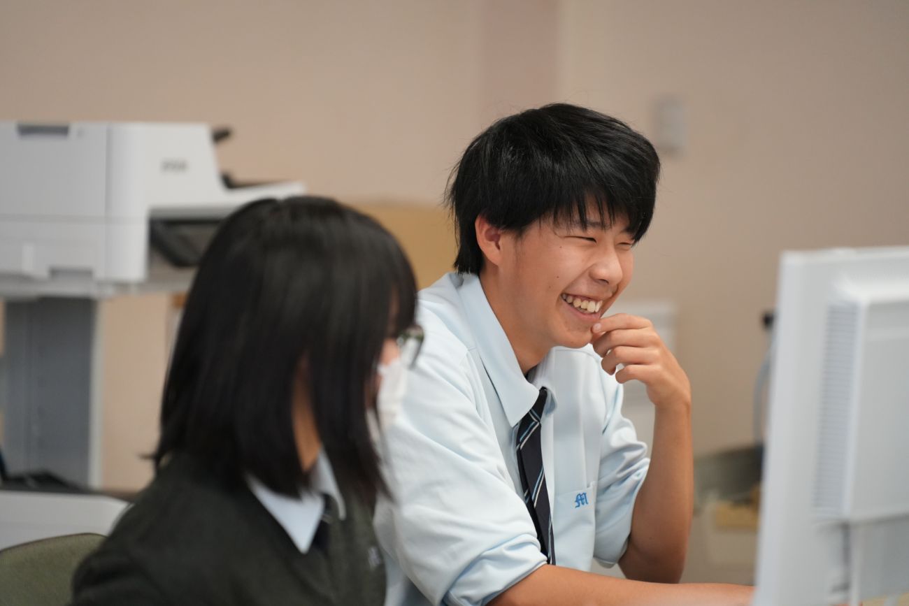 パソコン操作をしながら楽しそうに笑い合う男女の高校生が協力して作業している様子の写真
