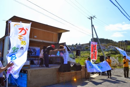 ステージの両側に設置された旗がなびく中、ステージ上で受賞者に賞状が授与されている様子の写真