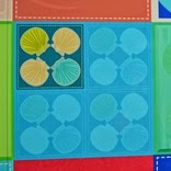 青や水色のカラフルな背景の上に、ホタテの様な形が円形に4つずつ配置された四つの区画があり、左上は黄色、右上と左下はベージュ色、右下は青色の模様が描かれているデザインをアップで写した写真