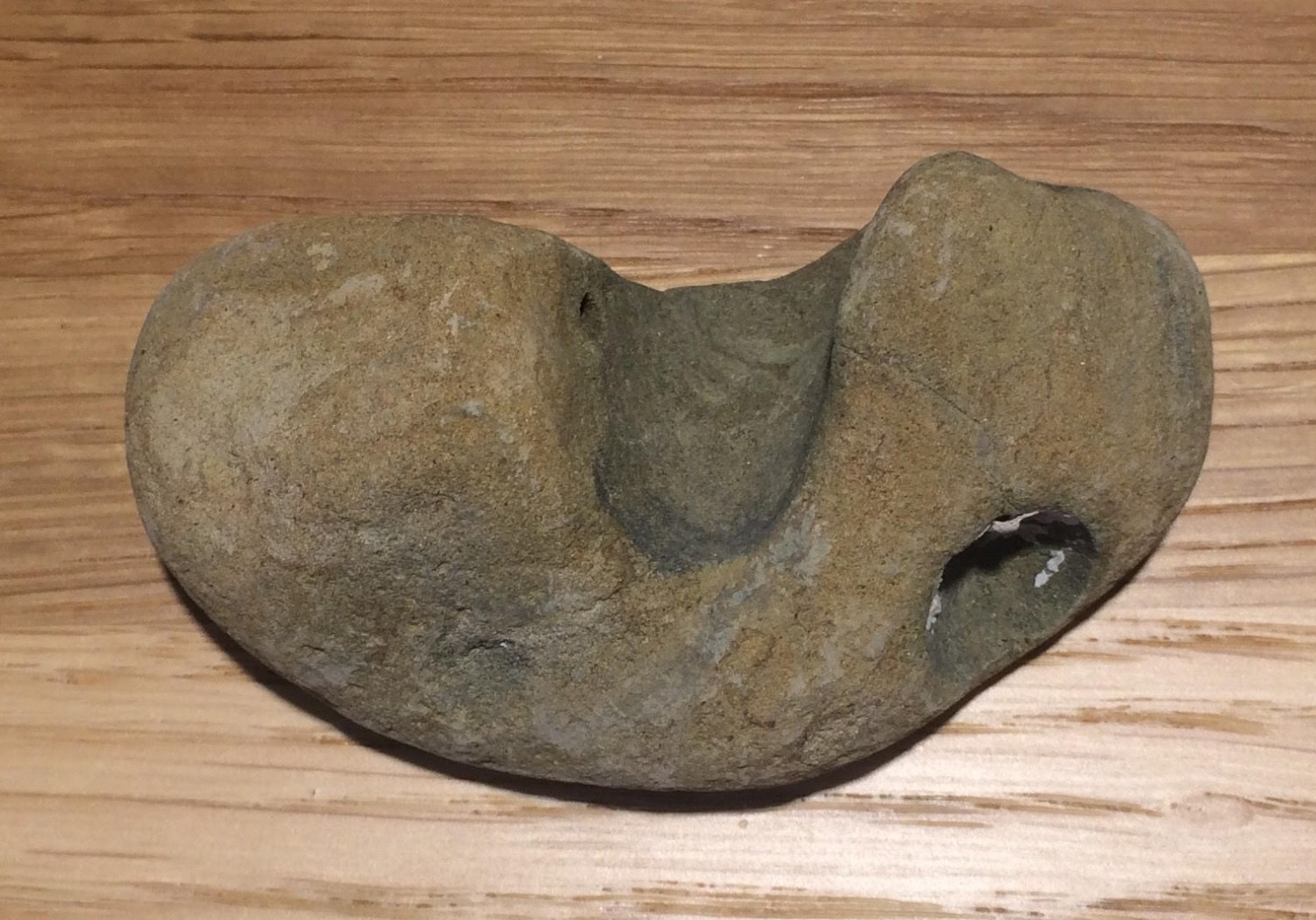 表面が滑らかで中央部分が大きくへこみ、右下に窪みのある不規則な形をした石が木目調のテーブルの上に置かれた写真
