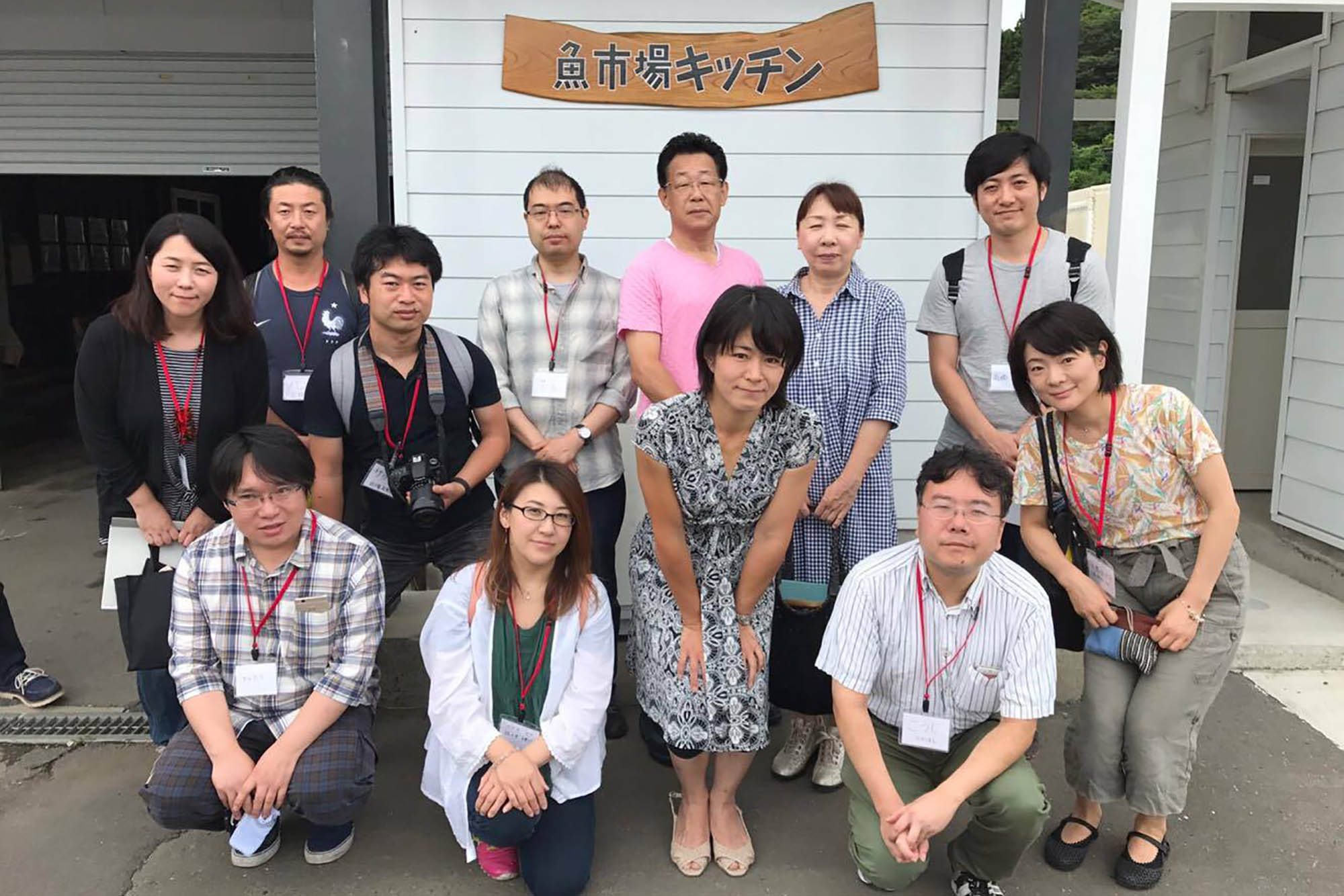 「魚市場キッチン」の看板の前で12人が集まって写した集合写真