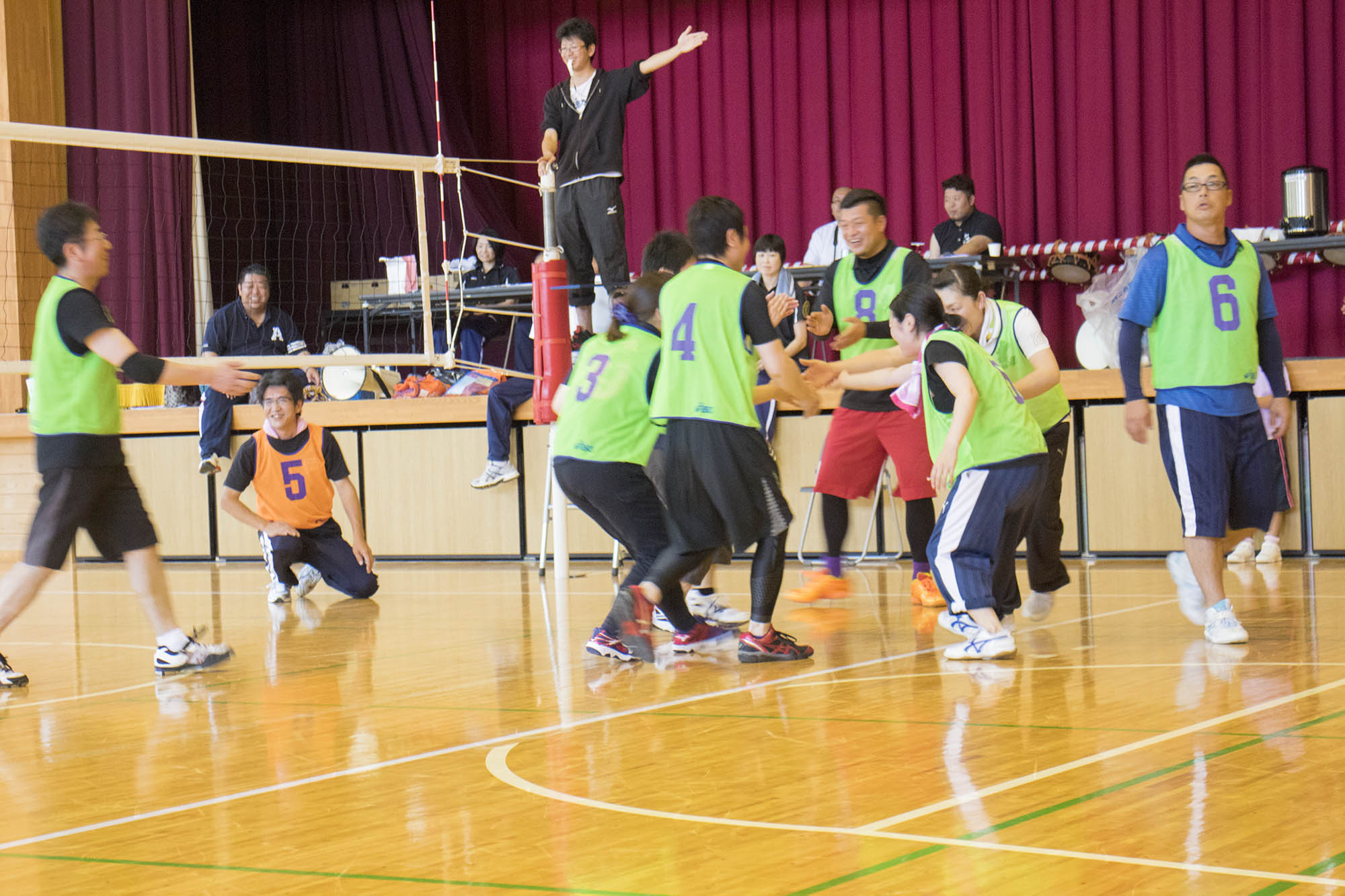 審判が左手を横にあげている中、緑のビブスを着たチームの選手たちが互いにハイタッチをしながら喜んでいる写真