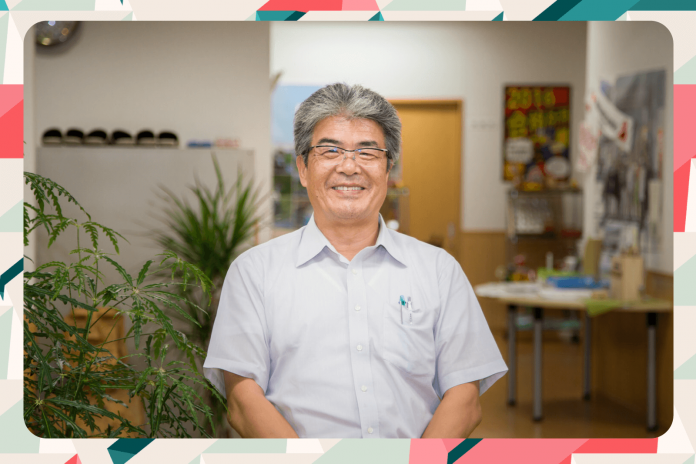 観葉植物が飾られた室内で、白い半袖シャツを着た山内松吾校長が笑顔で正面を向いている写真にカラフルな縁取りがされている画像