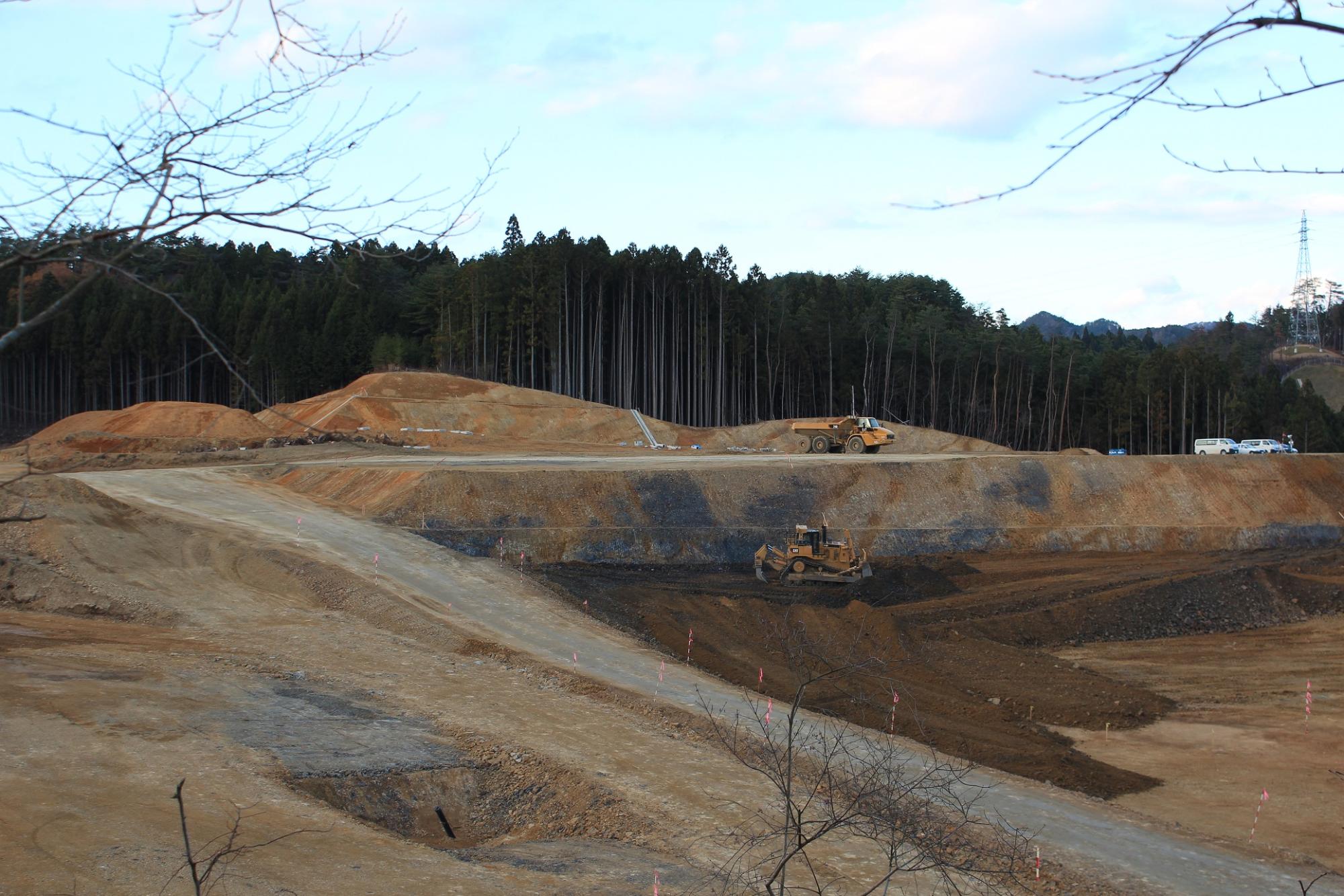造成地を取り囲むように、背後に元の自然の木々が山の稜線を描き造成された土地に入るスロープができている写真
