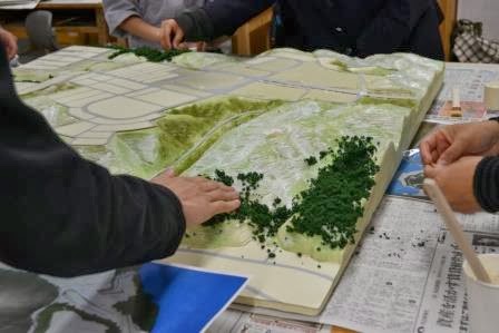 模型の山の部分に手作業で緑の樹木素材を貼り付けて森林部分を作っている途中の写真