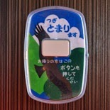 モクモクと浮かぶ雲に緑の木々と、大きな翼で飛ぶ鳥がデザインされ、「つぎ とまります」「お降りの方はこのボタンを押してください」と書かれた、降車ボタン装置をアップで撮影した写真