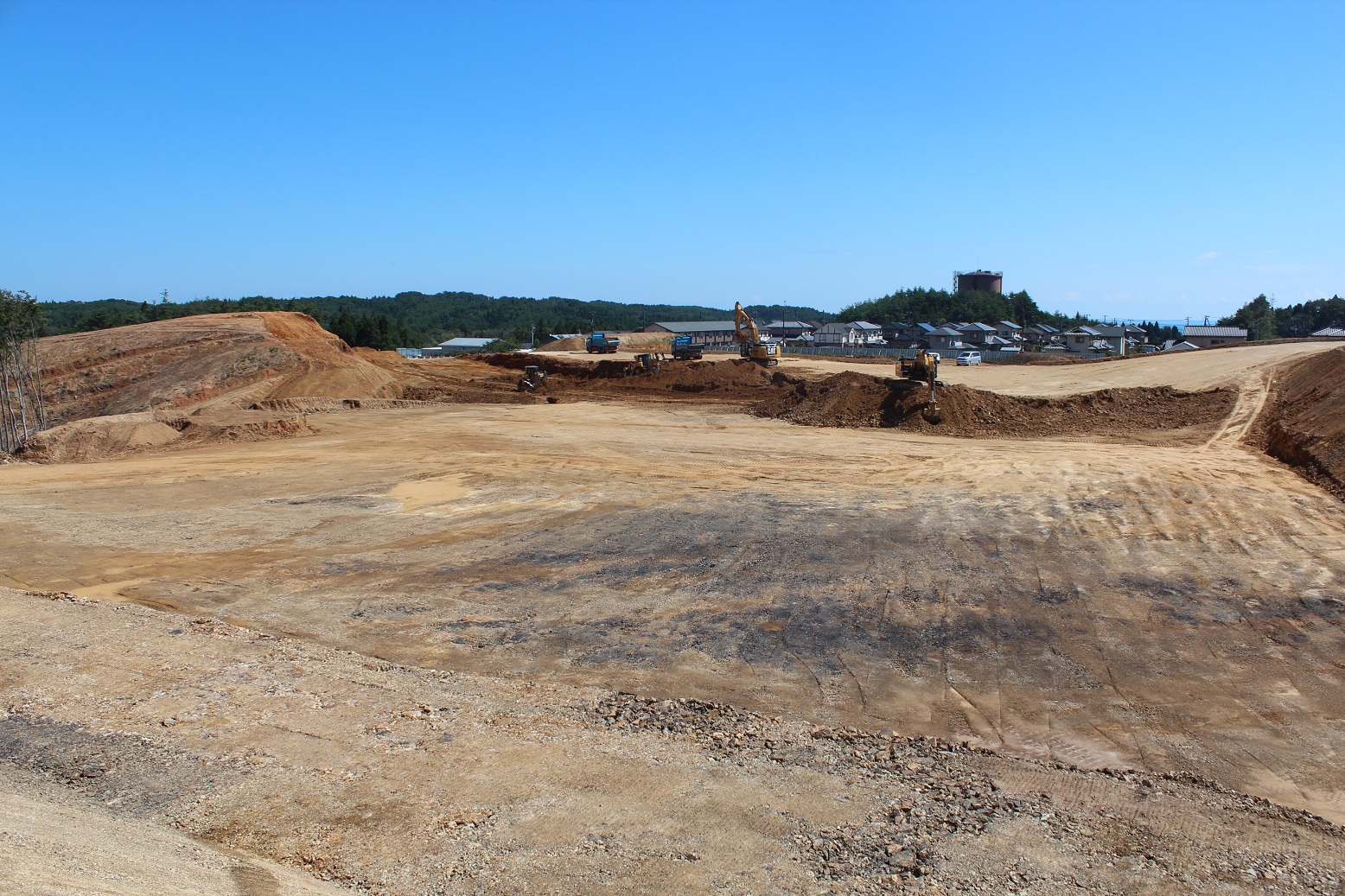 広大な土地が整地され、背景には建設機械や遠くの丘陵地帯が見える写真