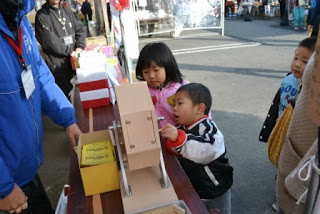子どもたちが商店街のくじ引きコーナーで楽しそうにガラガラ抽選器を回している様子の写真