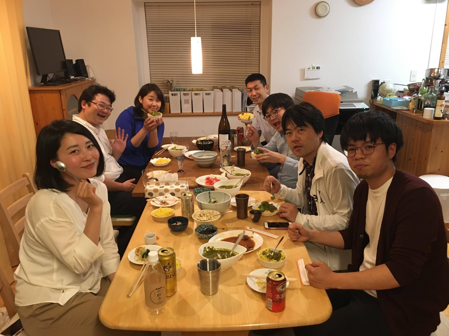 食卓を囲んで7人の男女が食事を楽しみながら笑顔を見せているホームパーティーの写真