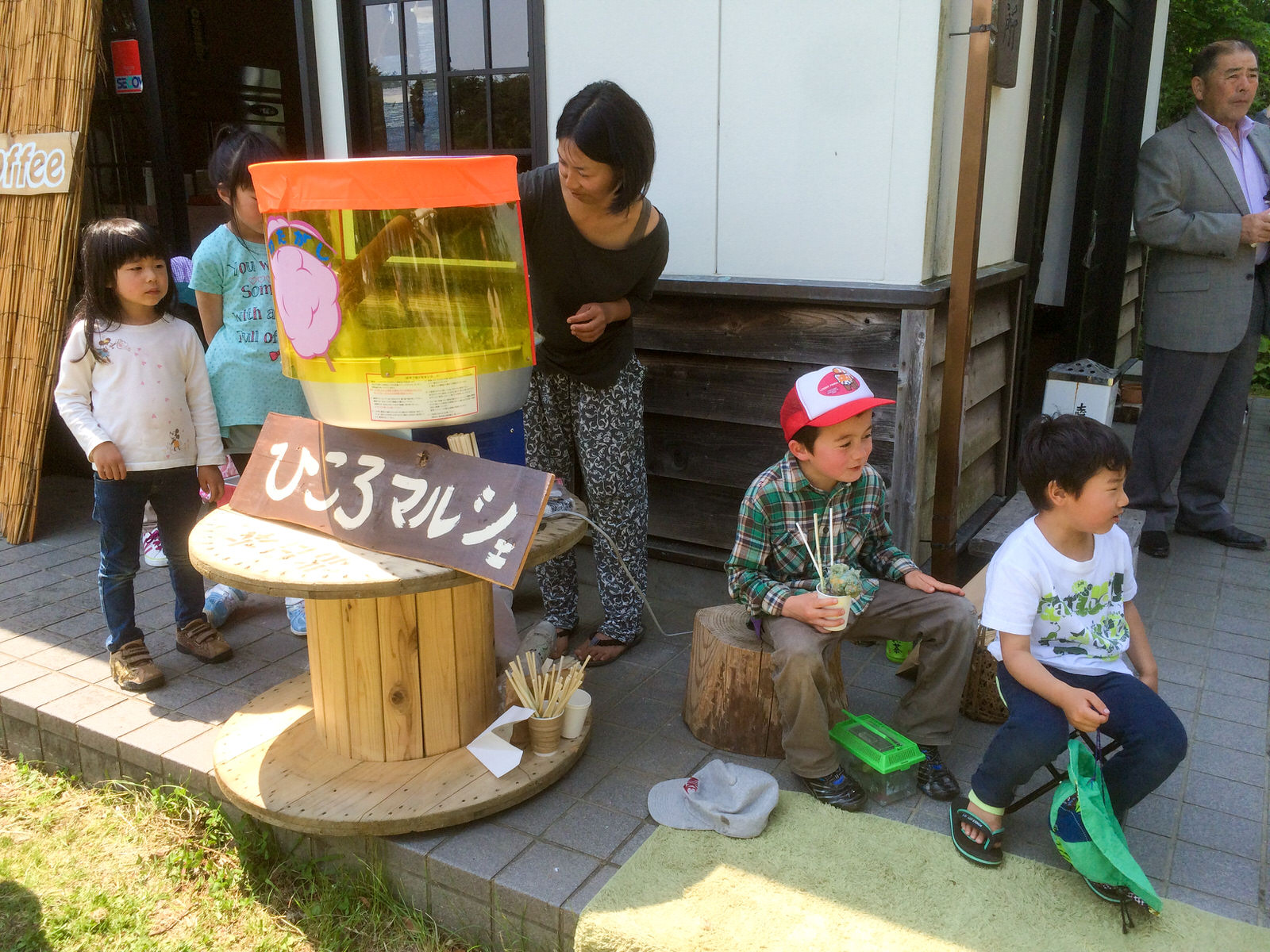 「ひころマルシェ」と書かれた看板のある綿菓子機のまわりに数人の子どもたちが楽しそうに集まり、女性が綿菓子を作っている写真
