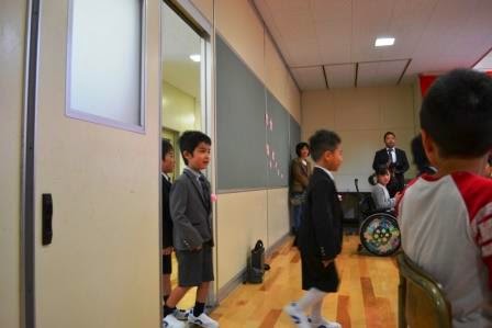先生方や在校生の児童たちが見ているなか、新入生の児童たちが多目的ホールに入ってくる様子の写真