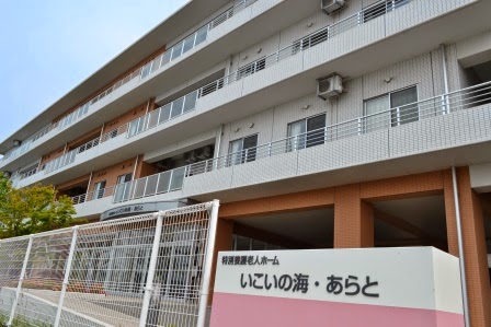 施設名が記載された看板と白いフェンスの敷地内に、白とレンガ調の外壁を持つ4階建ての建物外観の写真