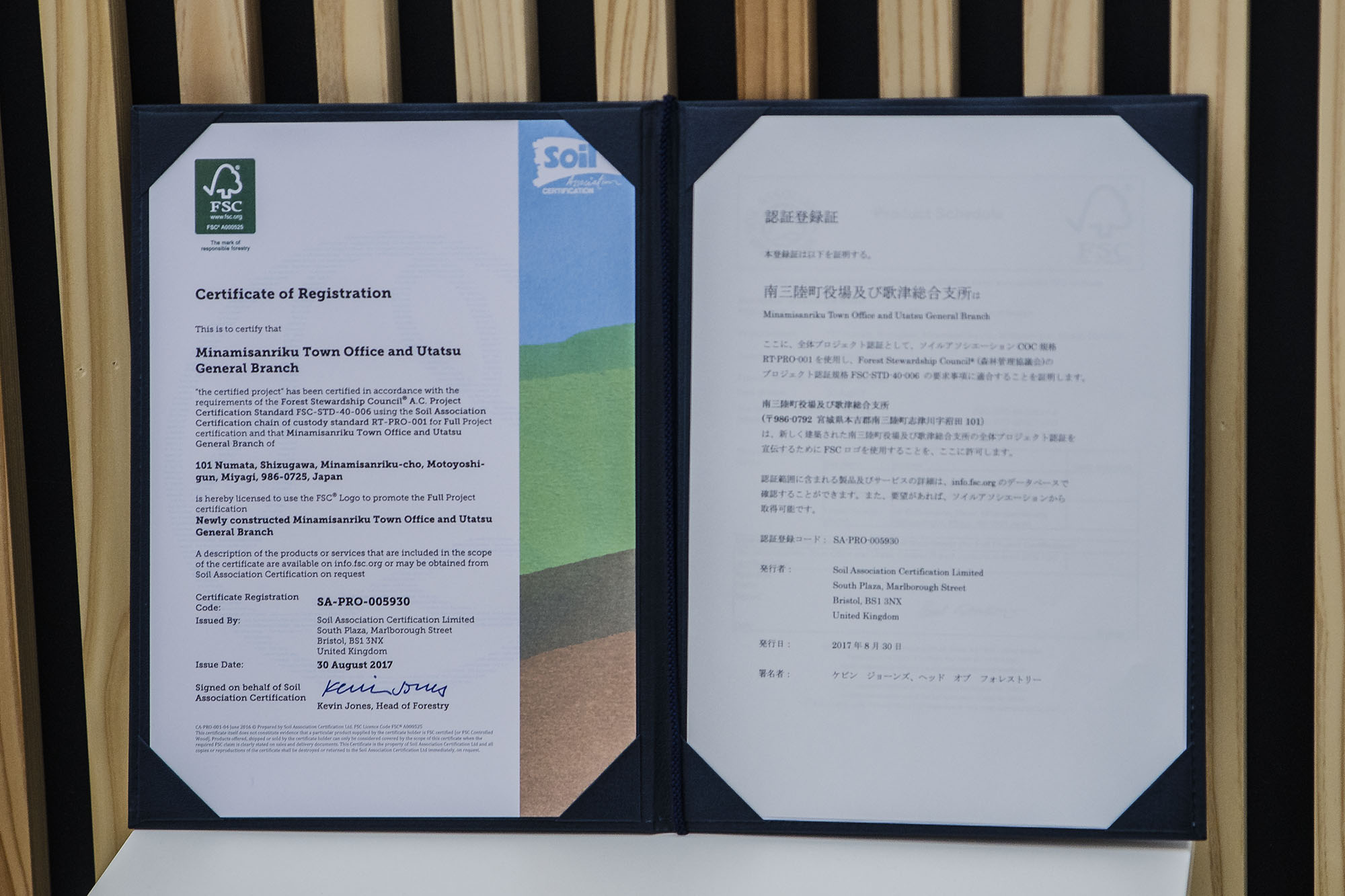 認証登録書が英語と日本語で書かれ開かれ、木の背板の前に立てかけて展示されている写真