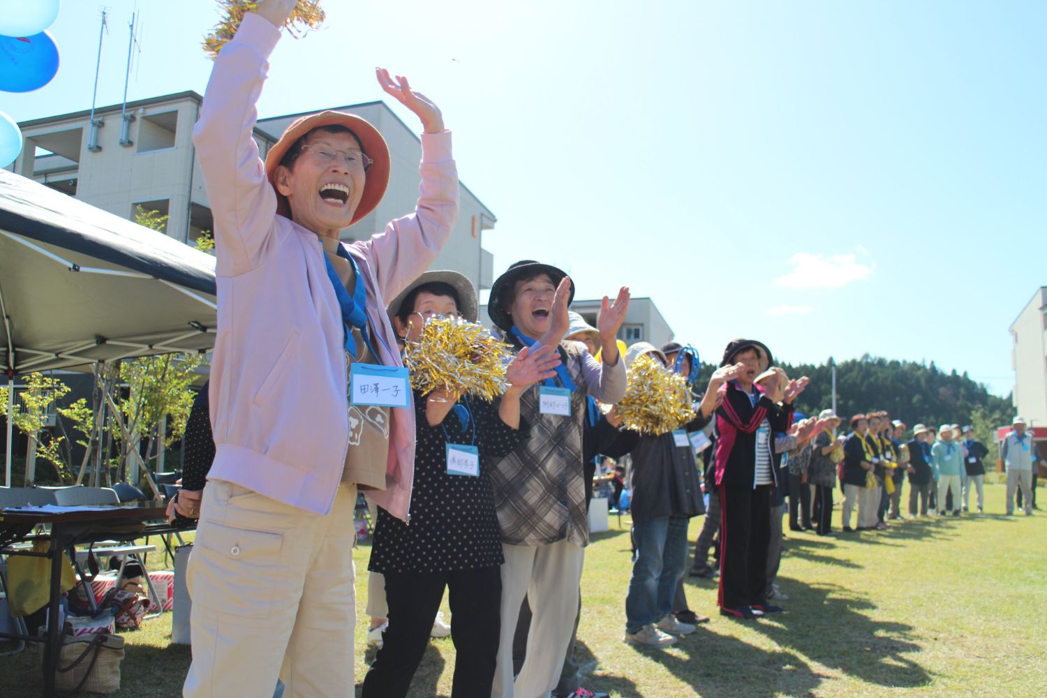 多くの人々が集まって応援しており、手前の女性が手を挙げて喜ぶ様子の写真
