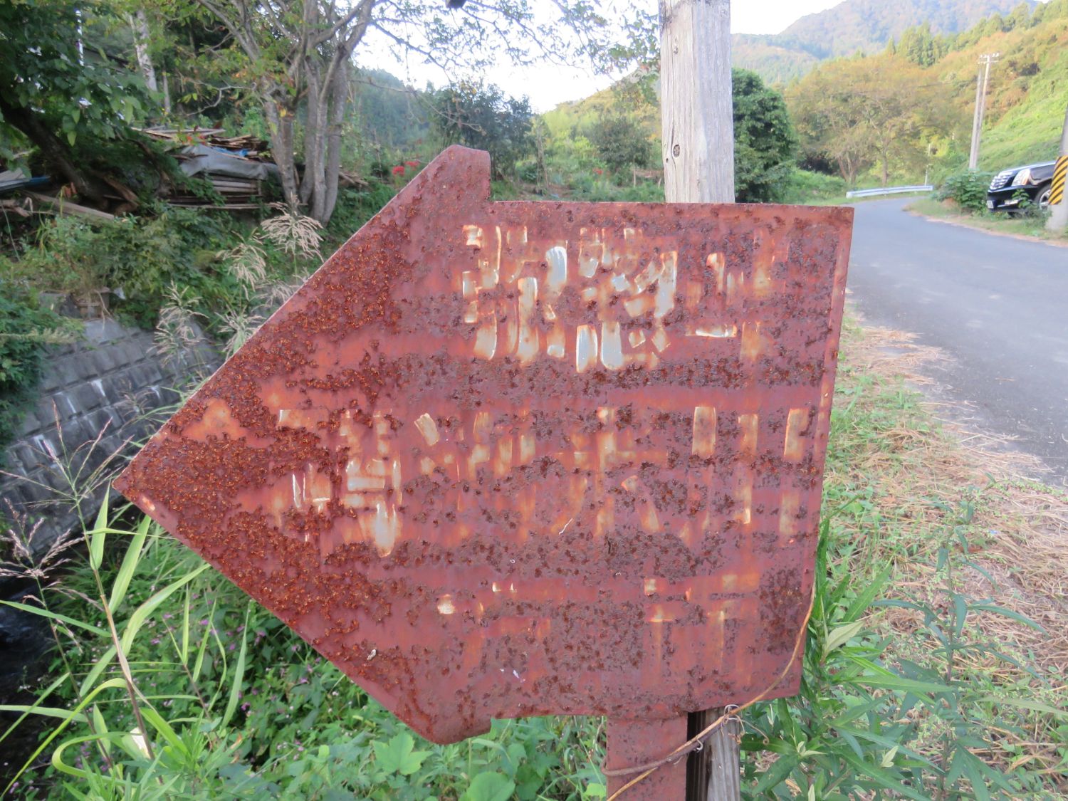 錆びついた矢印型の看板が立っている写真