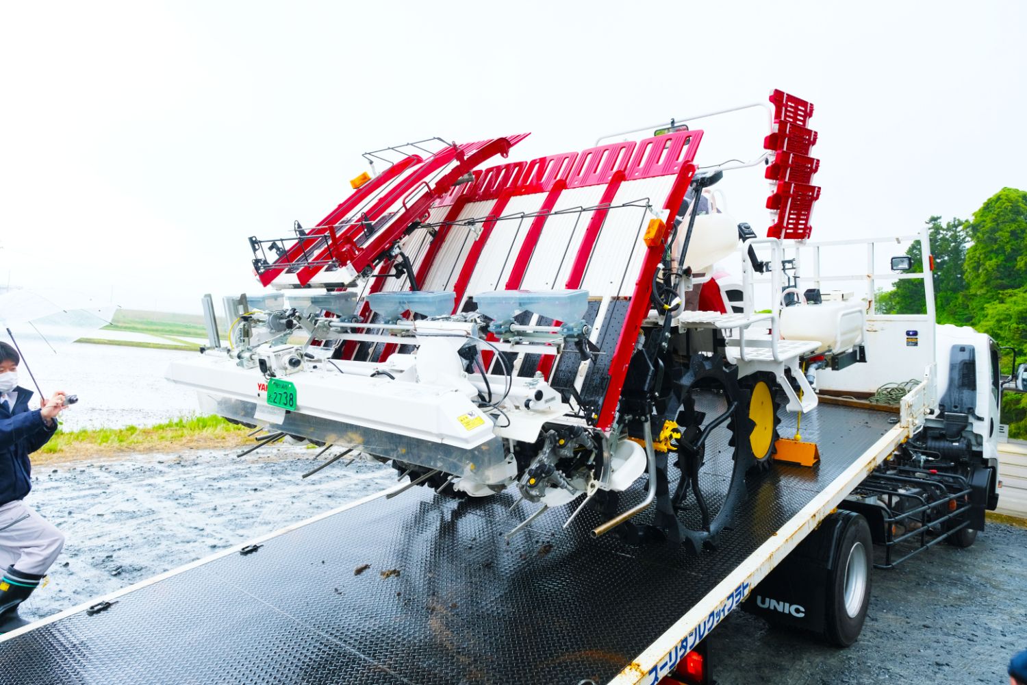 赤と白の複雑な構造の農業用機械がトラックの荷台に載っている写真