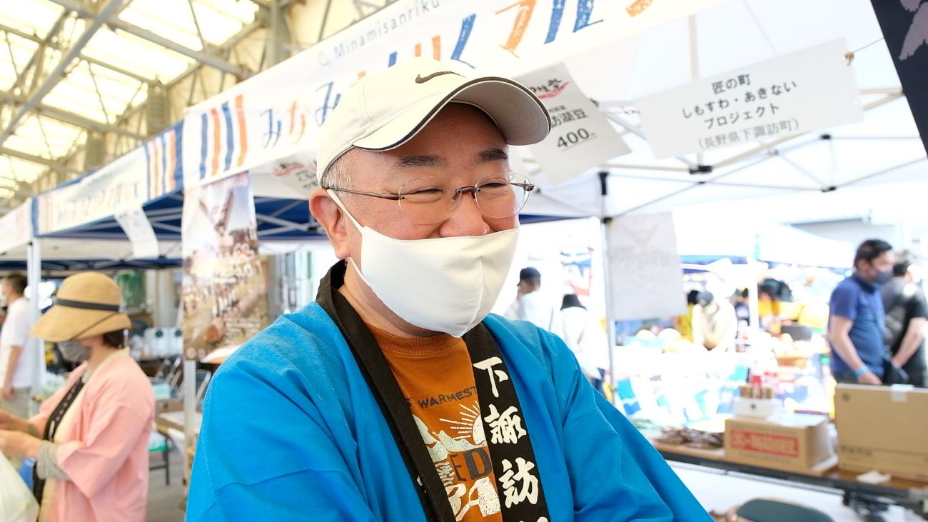 水色の法被を着た原雅廣さんが、笑顔でインタビューに答えている写真