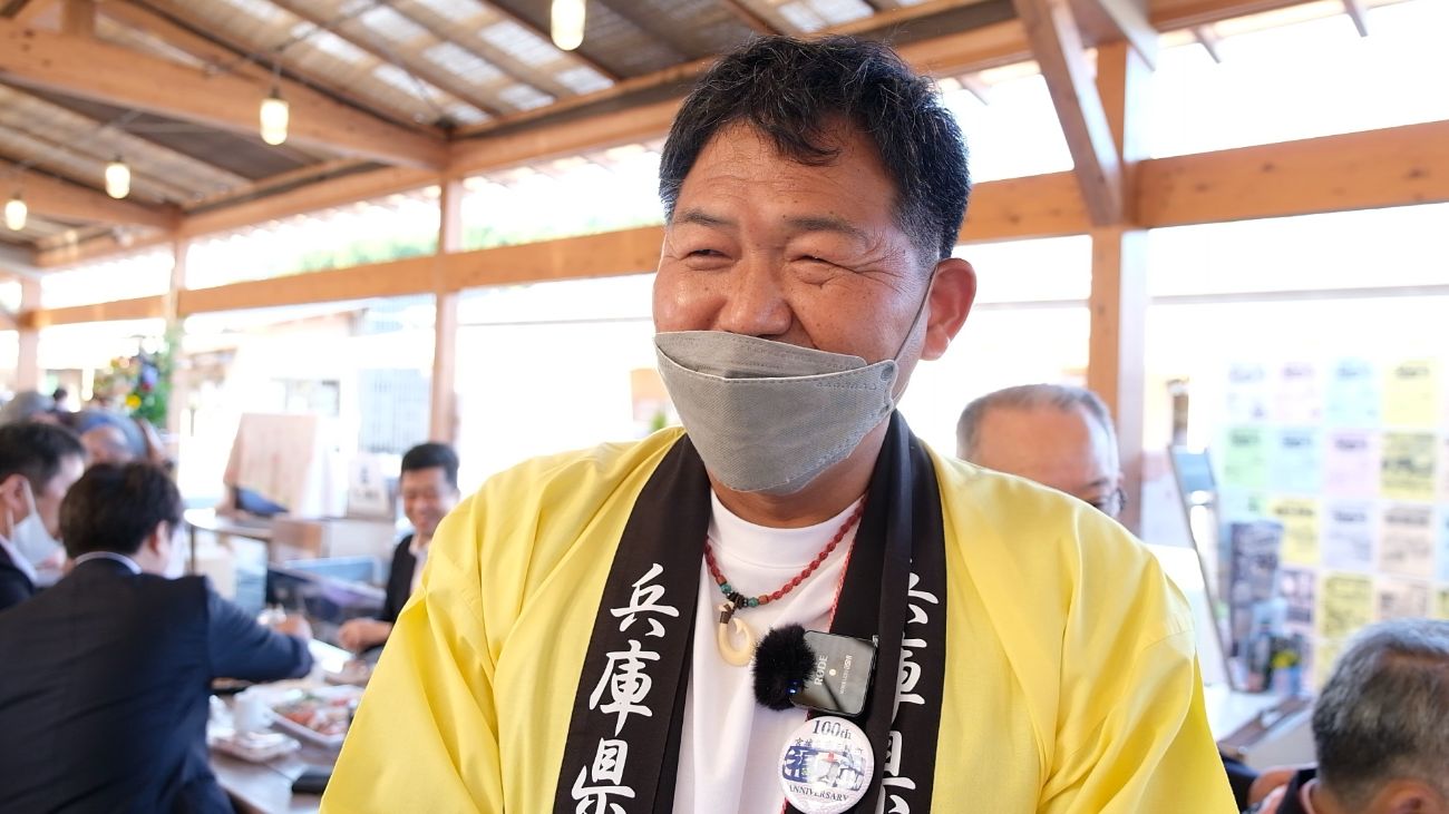 黄色の法被を着た千種和英さんがマスクをしながら笑顔で話している様子の写真