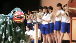 白いシャツと青い短パン姿の子どもたちが笛や太鼓を演奏し、獅子舞を披露している長清水鳥囃子（ながしずとりばやし）の郷土芸能発表の写真。