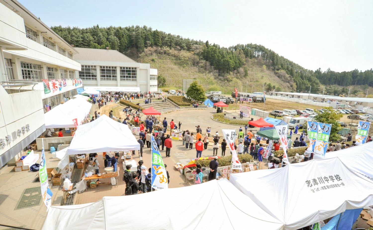 校舎の前にテントが並び、多くの人々が集まっている福興市の写真