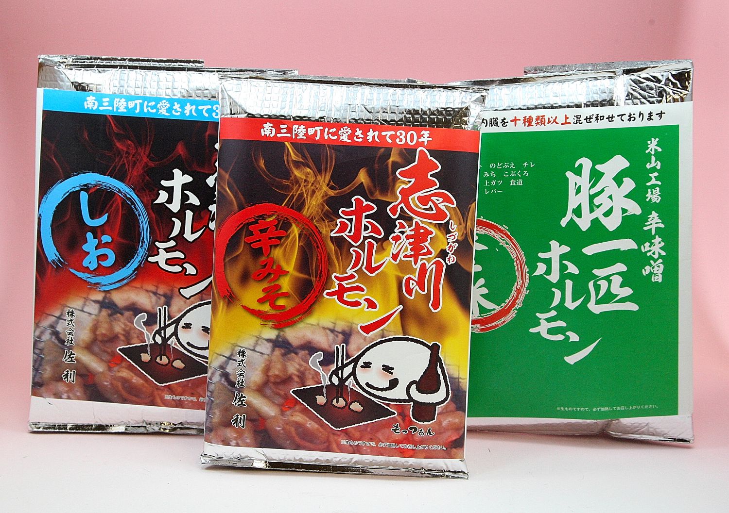 南三陸町で30年以上愛されている志津川ホルモンの3種類のパッケージで、赤の辛みそ味、青の塩味、緑の豚一匹辛味噌味が並べられている写真