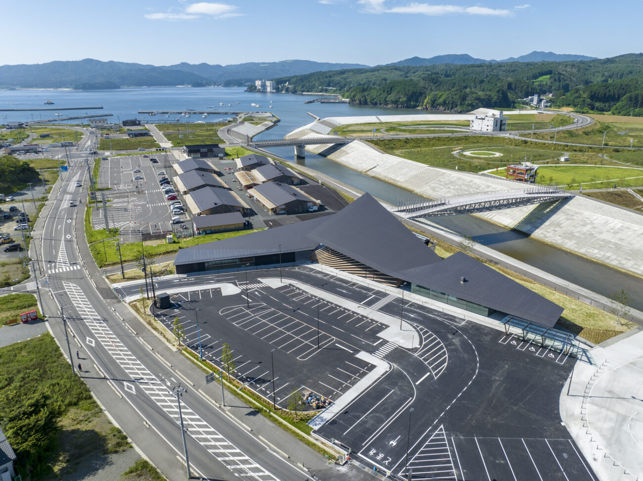 三陸の海沿いに建つ、黒い屋根が特徴的な「東日本大震災津波伝承館」の全景で、防潮堤や周辺のまちづくりとともに、復興の様子が見える航空写真