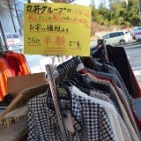 ハンガーラックに冬物の衣類が吊るされており、「半額」と書かれた手書きのセール案内が掲げられている様子の写真