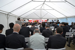 白いテントの中で多くの出席者が前方を向いて座り着工式に参加されている様子を後方から撮影した写真