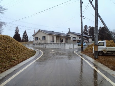 緩やかに曲がった舗装道路の先に、新築された平屋の住宅があり雨で道路が濡れている写真