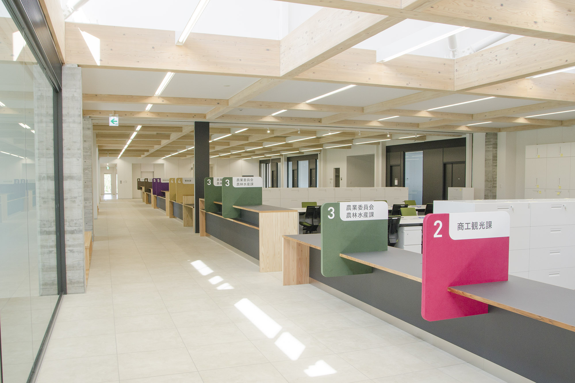 木材をふんだんに使った明るい庁舎内で、色分けされたカウンター番号と担当課名が表示された窓口が並んでいる通路の写真