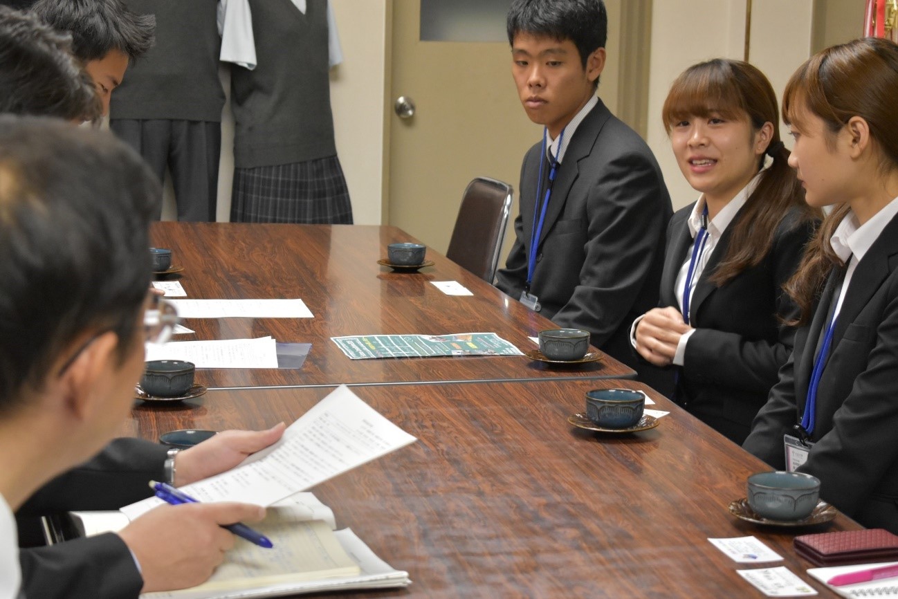 会議室でスーツを着た数人の人物が長方形のテーブルを囲んで座り、資料を前にして話し合っている様子が写っている写真