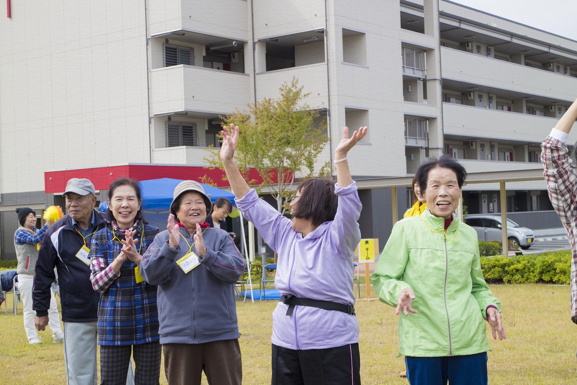 青空の下で縦一列の並んだ方々が拍手をしたり両手を挙げて喜んでいる写真