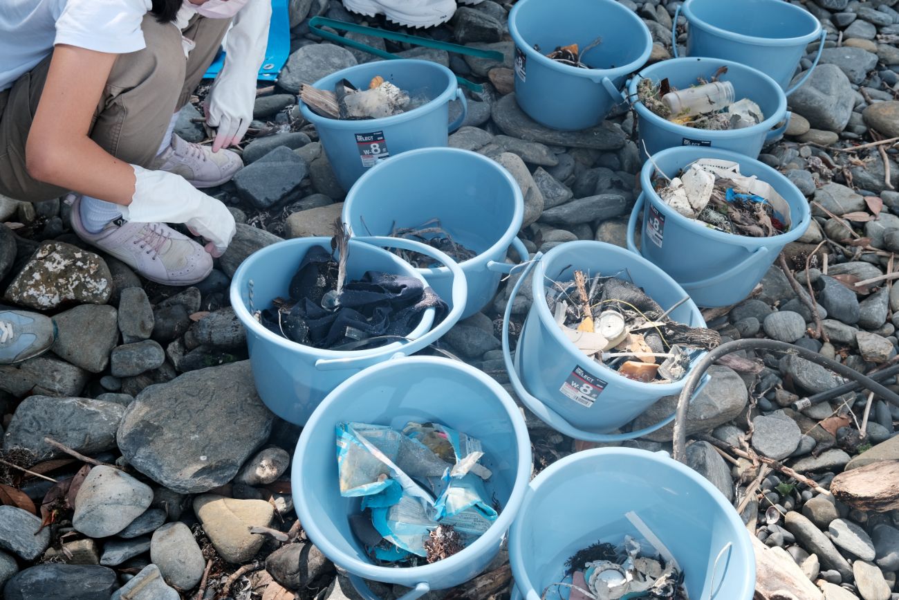 青いバケツがたくさん並んでいて、中にはプラスチック、空き缶、紐などさまざまなごみが入っている写真