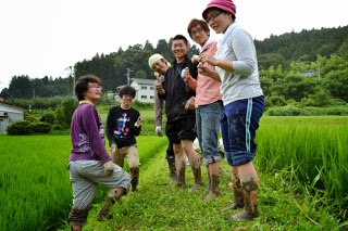 緑に色づいた稲が植えられた田んぼで参加した6名が足が泥だらけになって記念撮影をしている写真