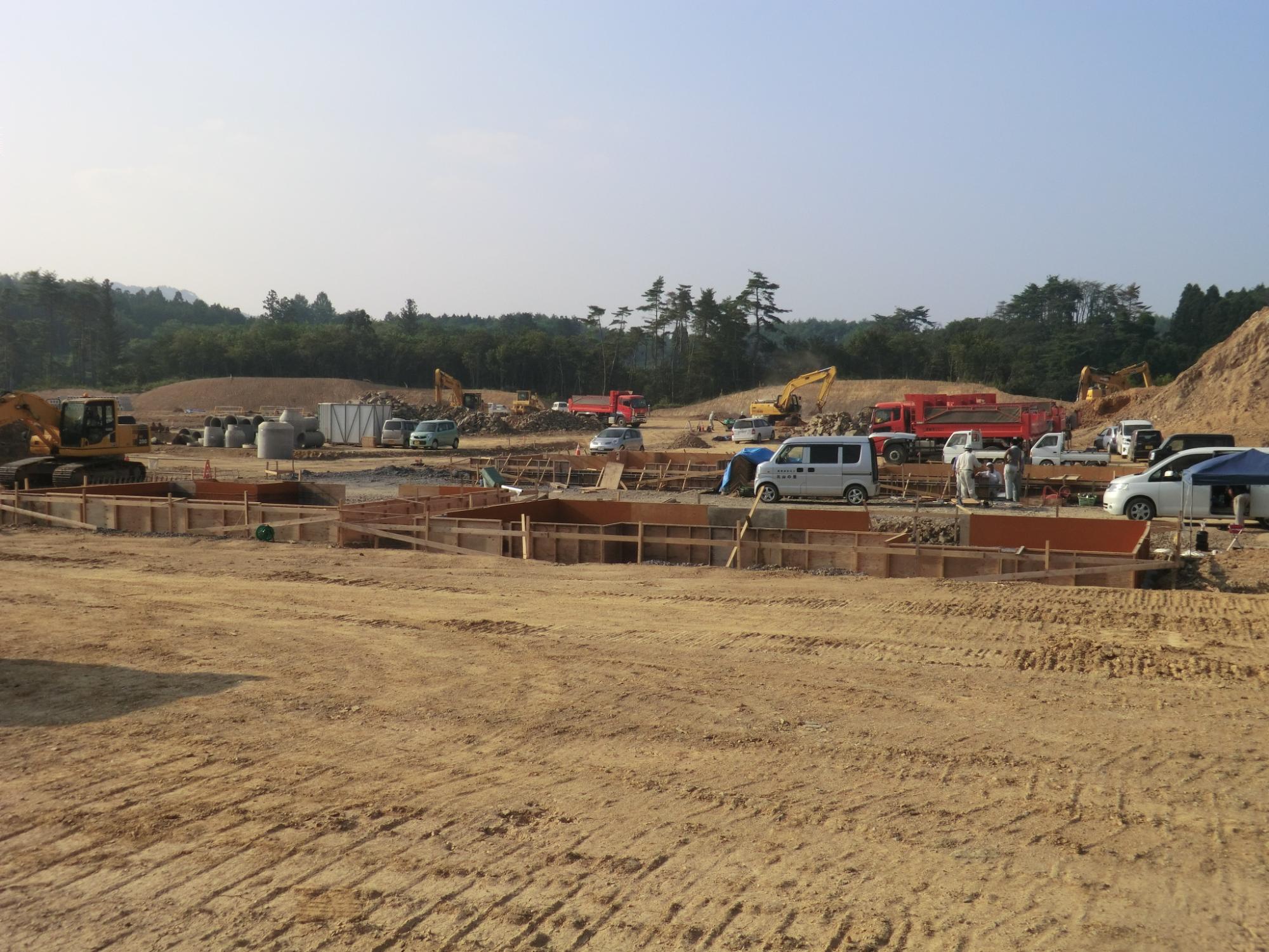 区画ごとに木枠で囲われた基礎工事が始まり人々が集まって活気ある建設現場の写真