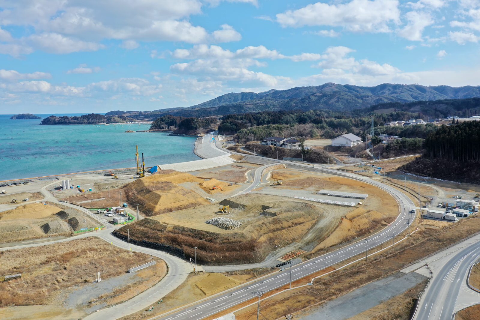 海岸沿いに連なる山々と、それに沿って整備された道路が見渡せる自然とインフラが調和した風景の写真