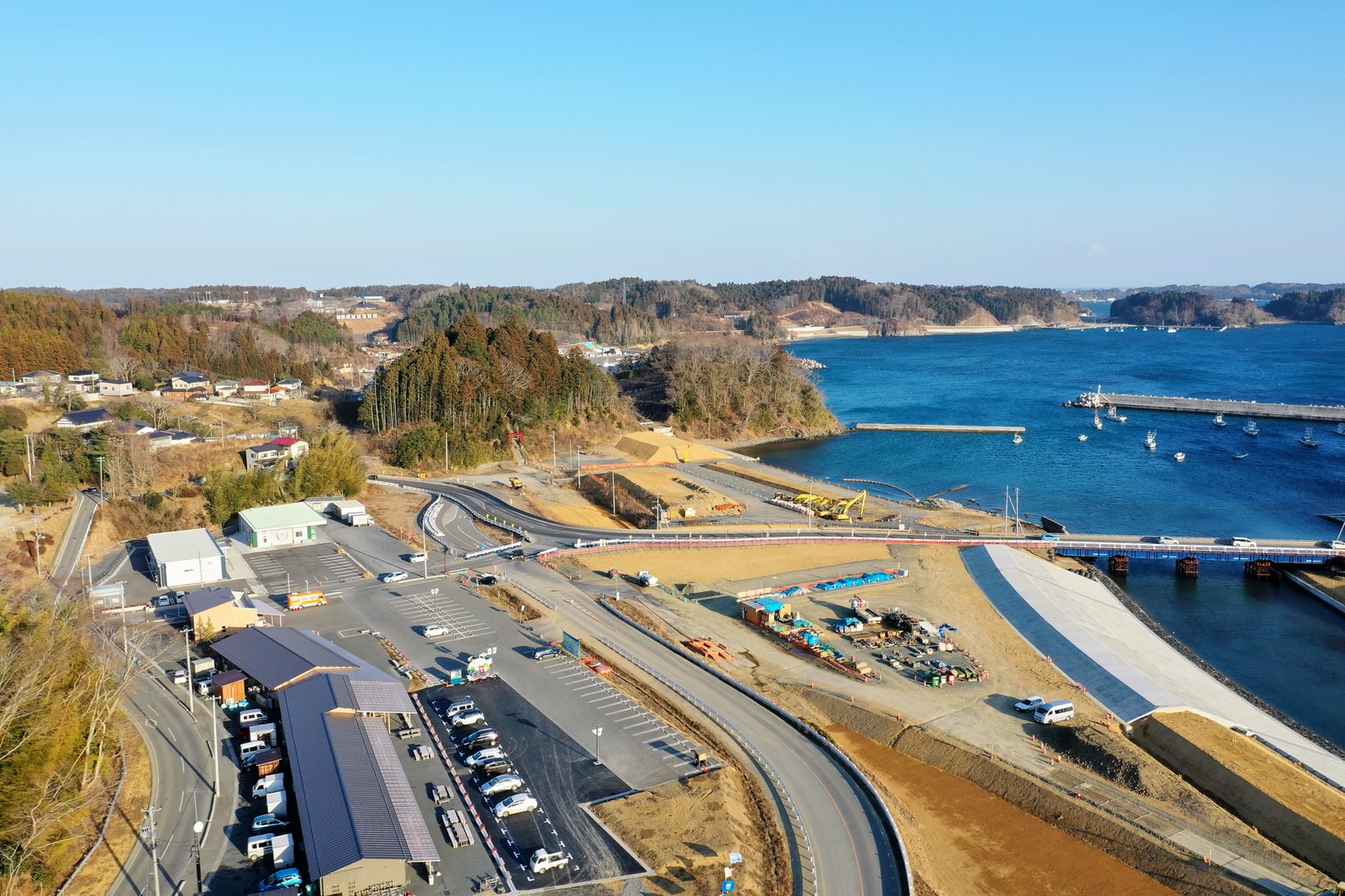 海岸沿いの町を空から見下ろした写真で、手前には駐車場と建物が並び、奥には広がる海と港が見える海辺の町の写真