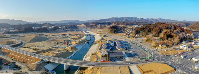 広大な土地に川が流れ、その川に橋が架かっていて、周囲には建物や道路が整備されている様子が一望できる風景の写真