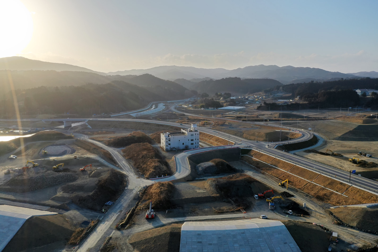 山に囲まれた地域で建設作業が行われている様子が見られ、重機や資材が配置されている山間部の建設現場の写真