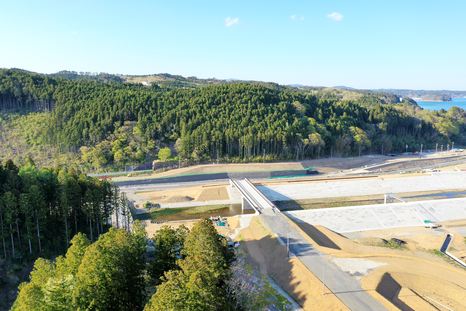 緑豊かな森林に囲まれた地域の中央に橋が架かり、その下を道路が通っている様子を空から撮影した山間の橋と道路の写真