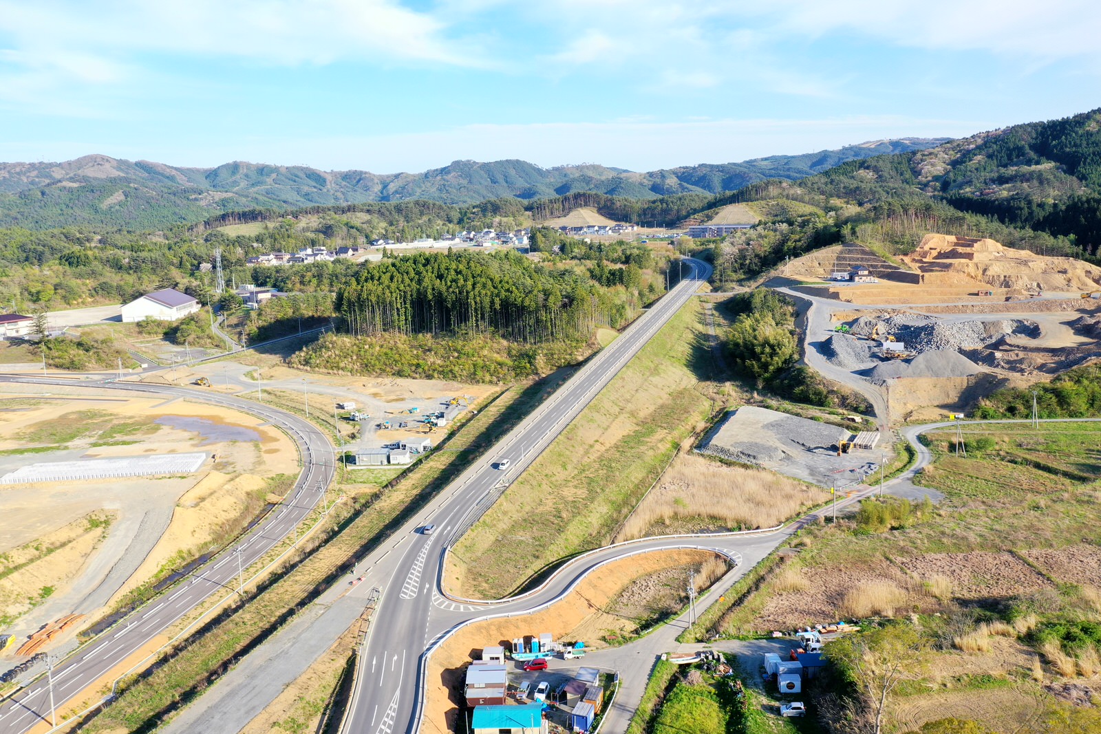 山間部にある道路が曲がりくねりながら緑豊かな地形を通り抜けており、その周囲には森林や斜面が広がる様子を上空から撮影した山間の道路の写真