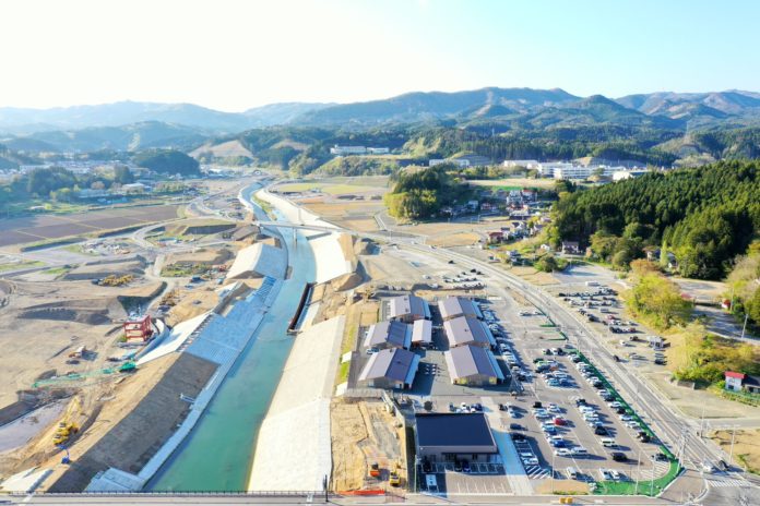 川沿いに広がる工事現場と駐車場の様子を空から撮影しており、周囲には道路や建物も見える川沿いの工事現場の写真